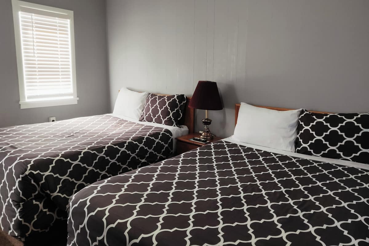 A bedroom with two beds, a nightstand, a lamp, and a window with blinds.