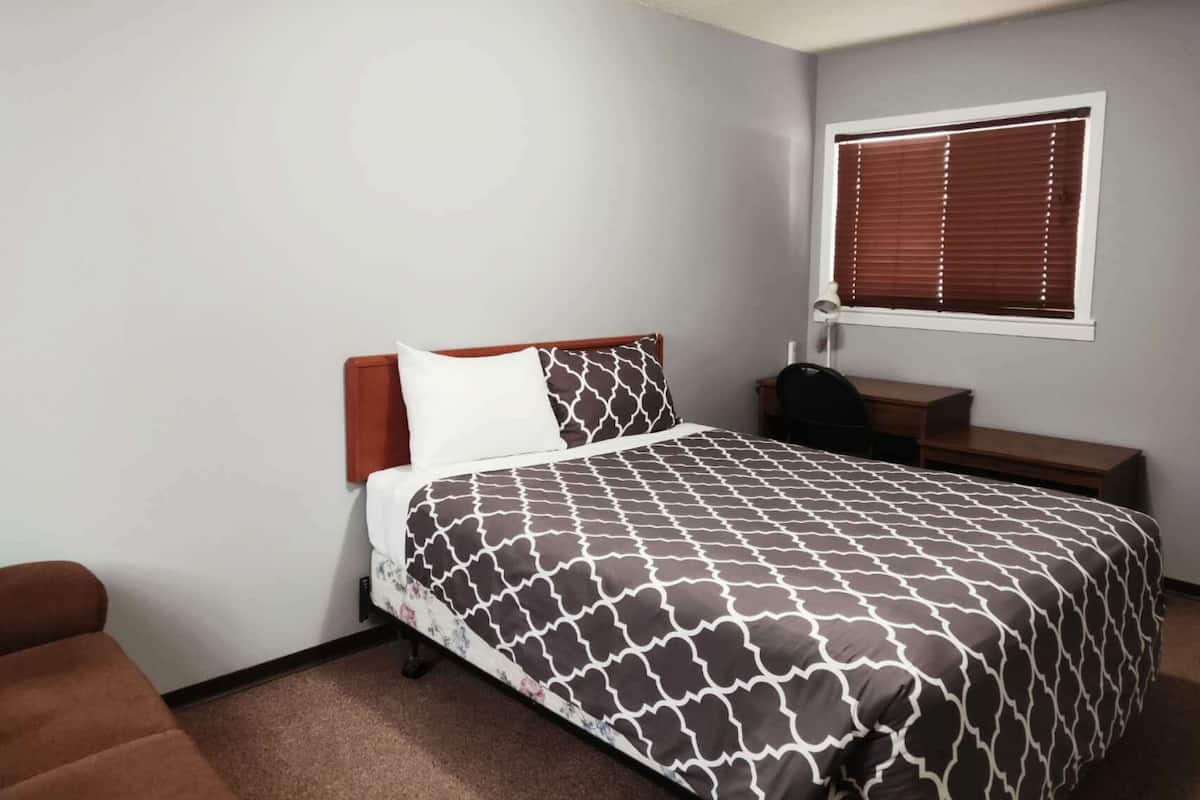 A bedroom with a bed, a desk, and a window with blinds.