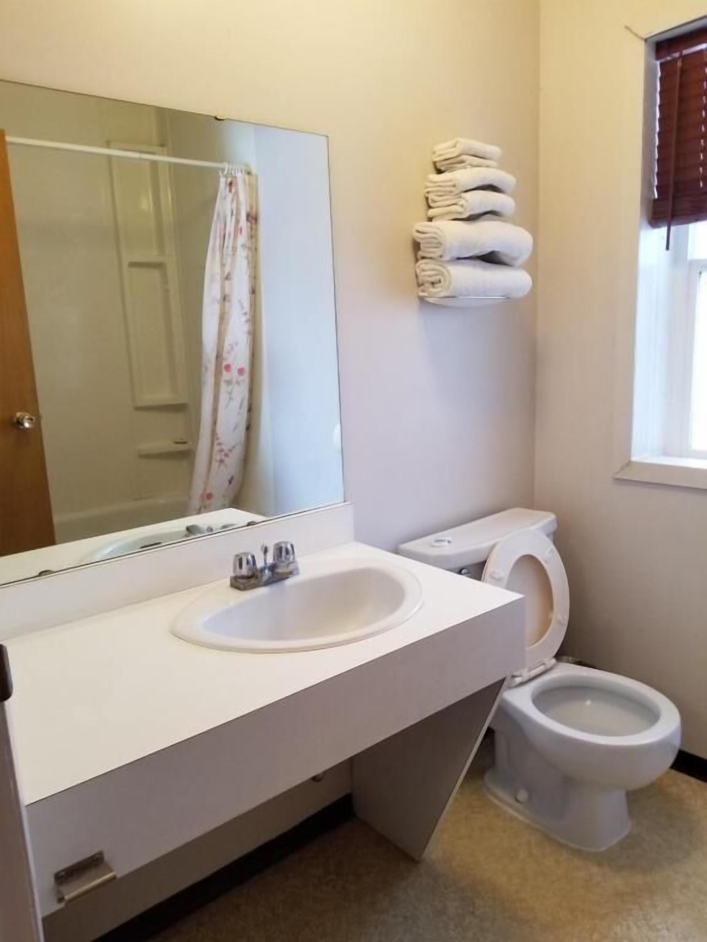 A bathroom with a white sink, a toilet, a mirror, and a stack of towels on the wall.