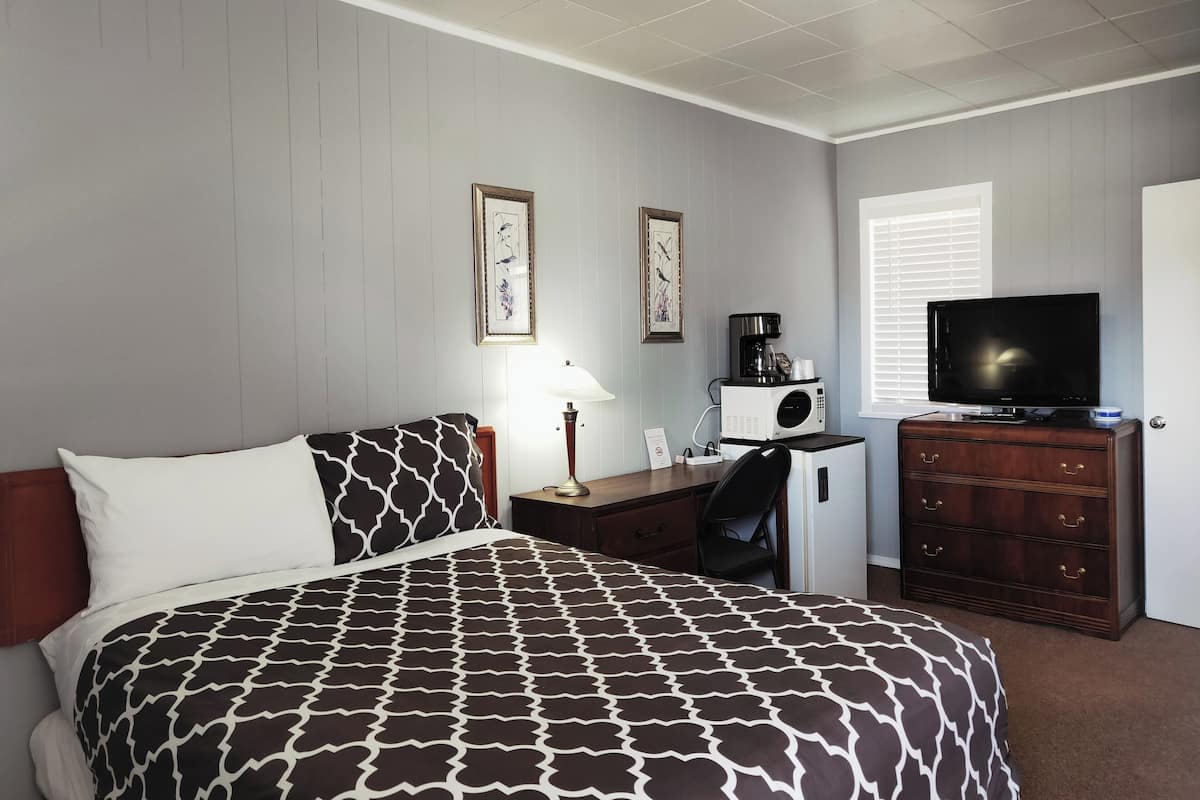 A hotel room with a bed, a desk with a coffee maker, a television, and a dresser.