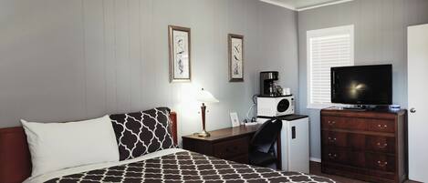 Habitación de hotel con cama, escritorio con cafetera, televisor y cómoda.