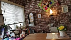 A reception area with a brick wall, a wooden reception desk, a window with blinds, a wall clock, and a wall-mounted light fixture.