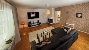 Una sala de estar con un sofá negro, televisor, chimenea y pared decorada.