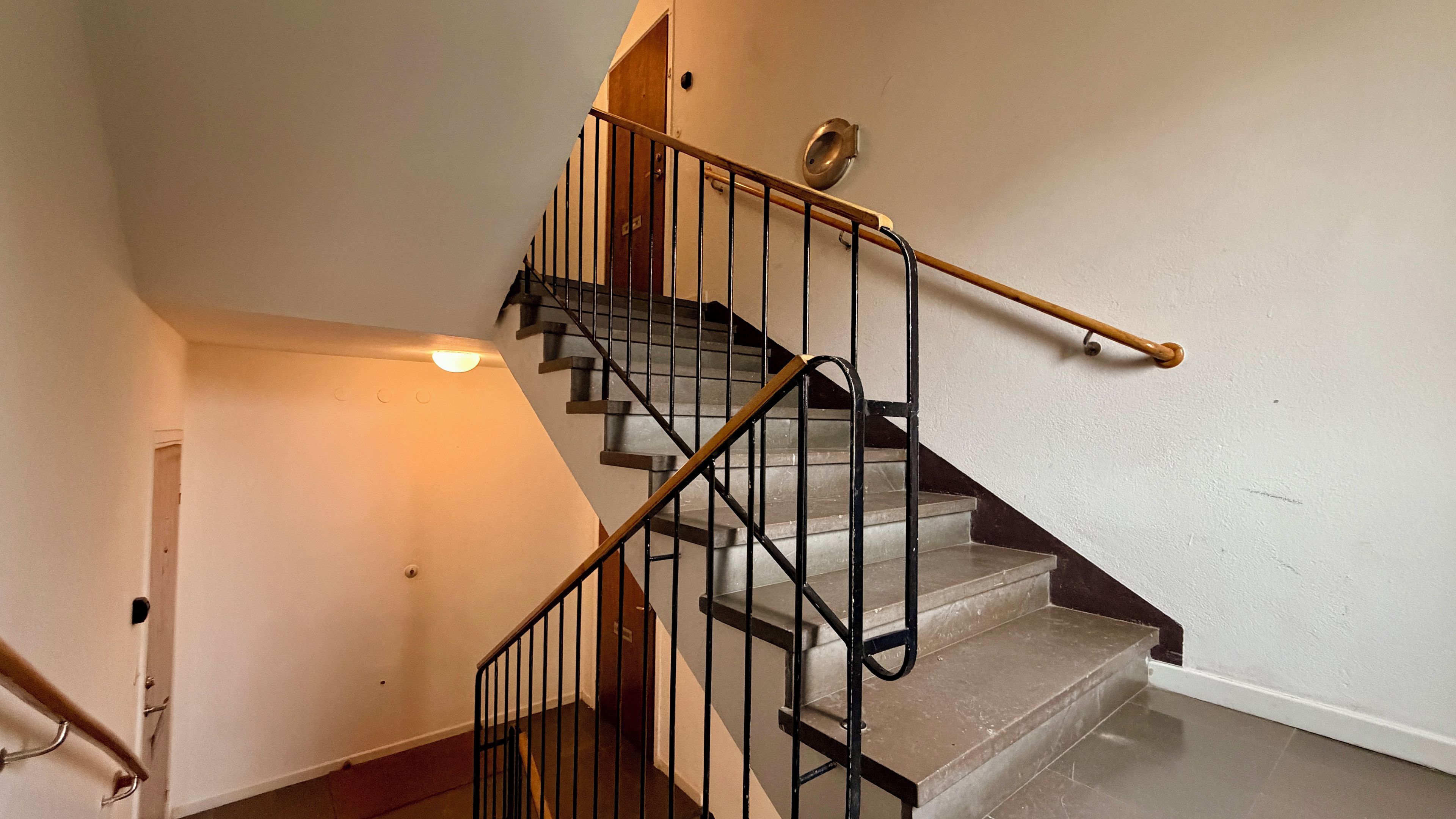 Una escala amb barana, una làmpada i una porta a dalt.