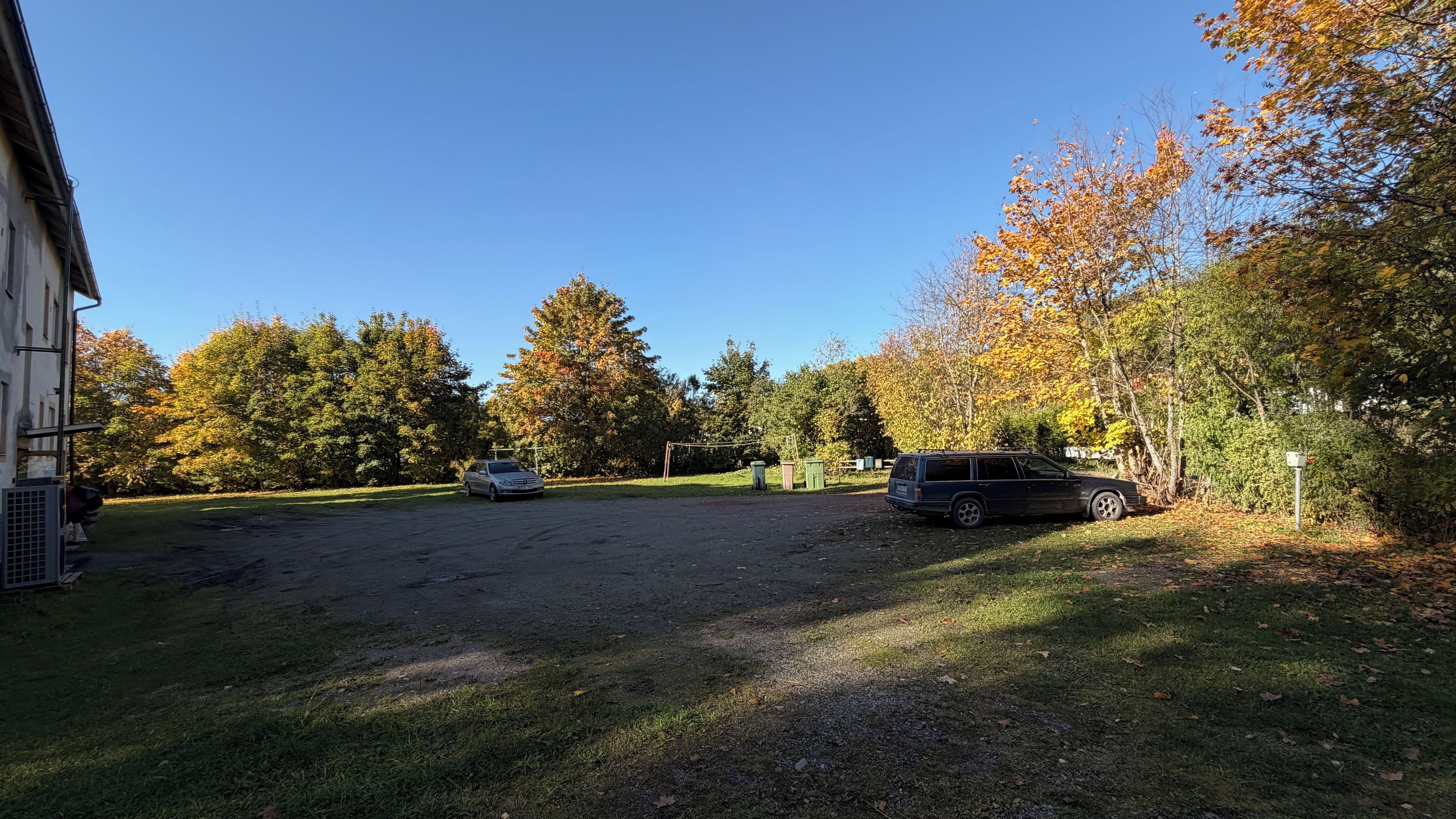 A parking area with two cars, a grassy field, and trees with autumn foliage.