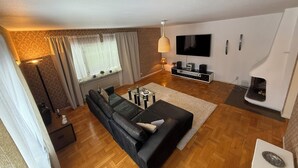 Una sala de estar con un sofá negro, un televisor, una chimenea y un muro con diseño.