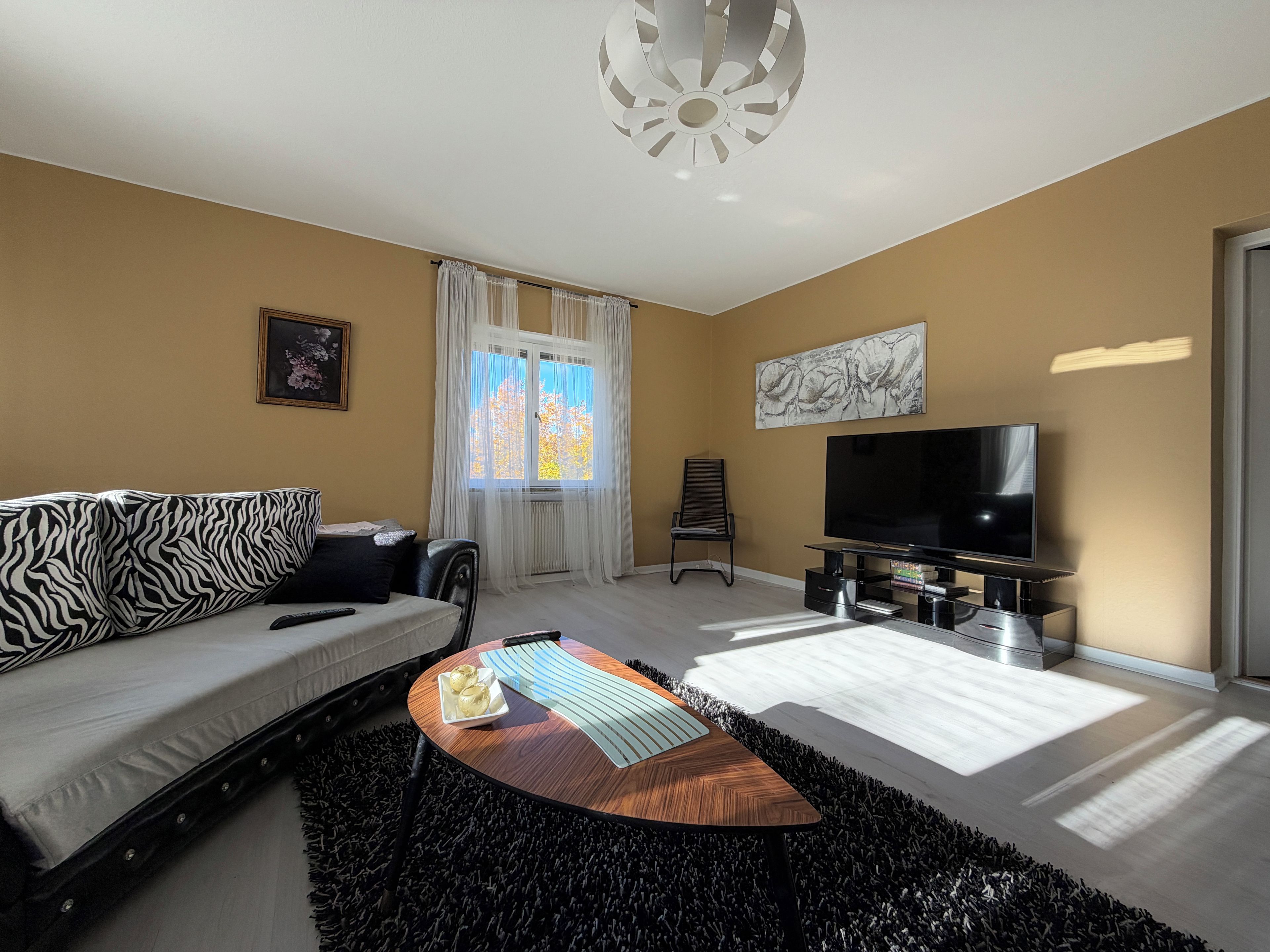 Una sala de estar moderna con sofá, mesa de centro, televisor y ventana con cortinas.