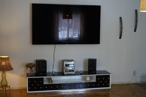Ein Flachbildfernseher an der Wand, eine schwarze Unterhaltungseinheit mit Lautsprechern und eine Lampe auf einem Beistelltisch.