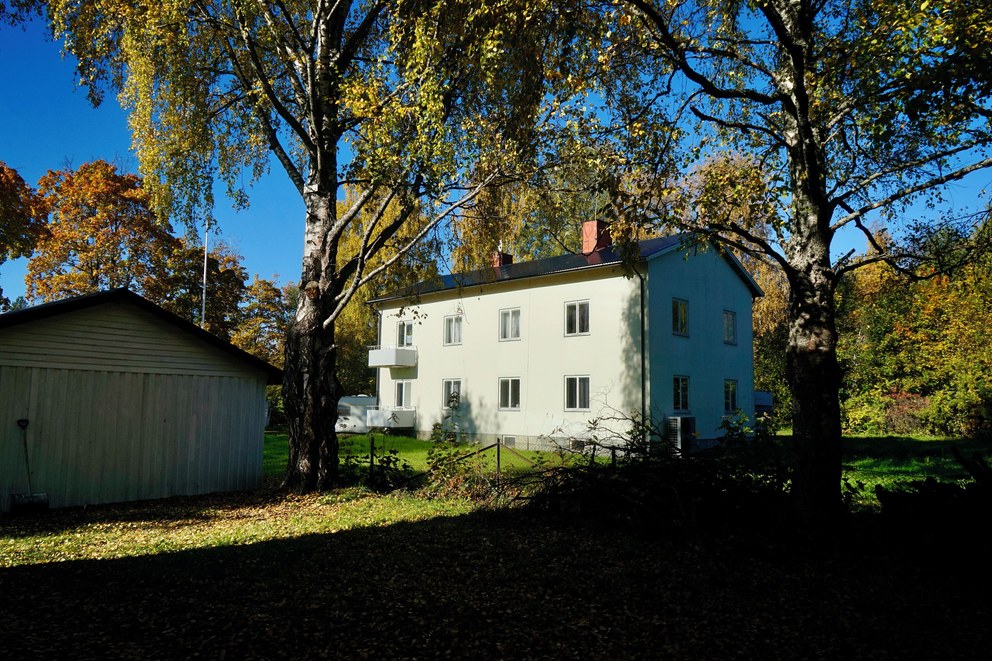 A two-story building with a flat roof, surrounded by trees with autumn foliage.