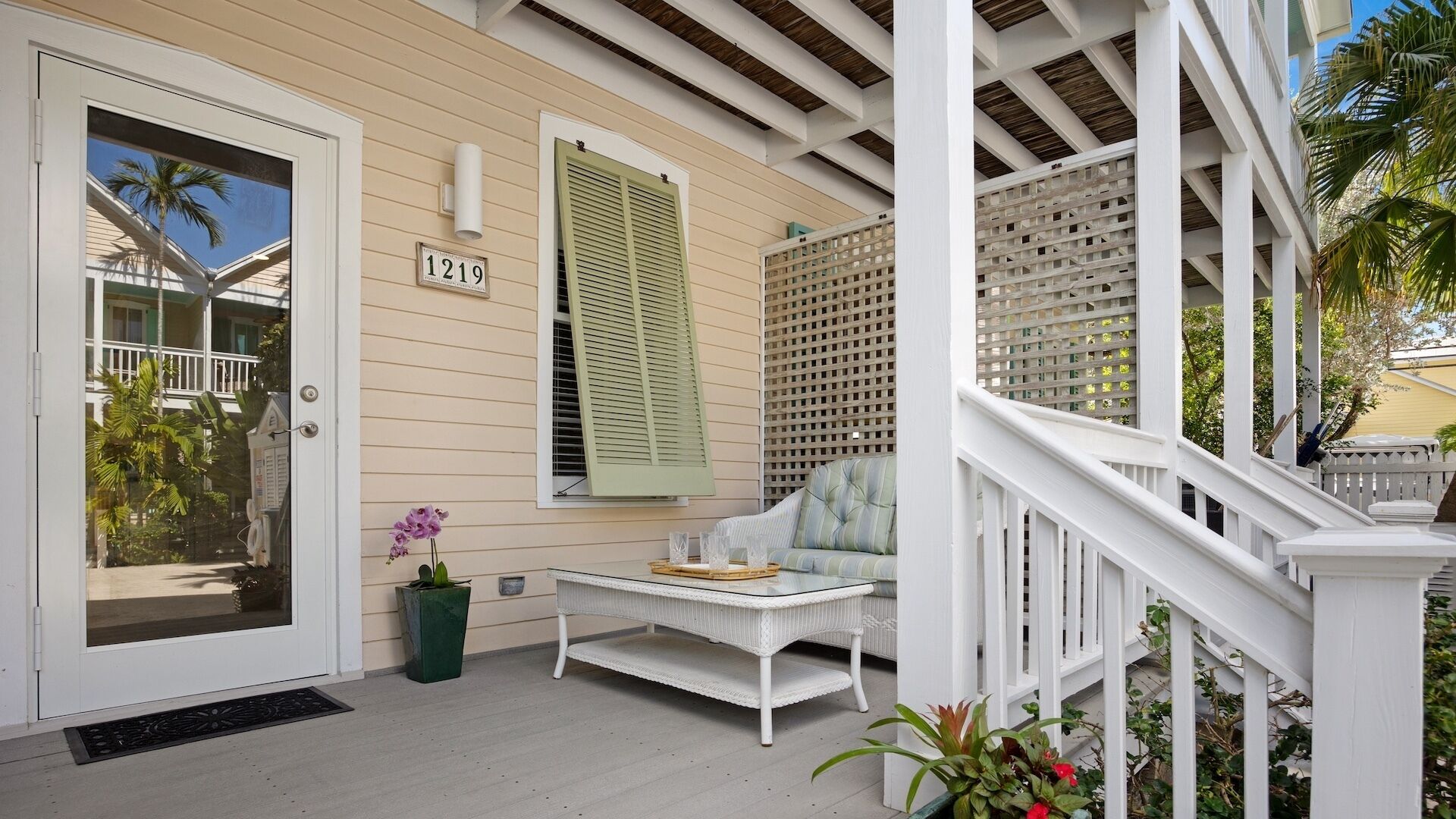 A porch with a white railing, a green planter, and a white sofa with a glass table.