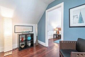 A room with a wooden floor, a black sofa, a framed picture on the wall, and a shelf with decorative items.