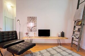 Un salon moderne avec un canapé en cuir noir, une table basse en bois, un téléviseur à écran plat et un tapis à motifs.