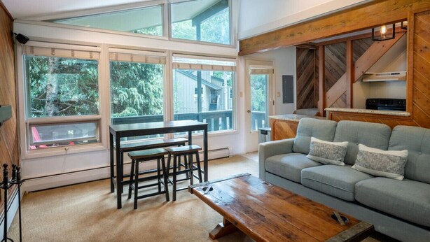A living room with a sofa, a wooden coffee table, a dining table with chairs, large windows, and a herringbone-patterned wall. - Local`s Condo in Vail, Steps from Ski Shuttle (Vail)
