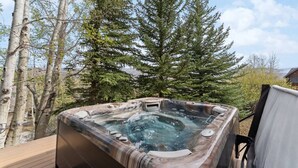 A hot tub in an outdoor setting with a wooden deck, surrounded by trees. - Gold Dust Getaway | Hot tub | Near Ski Resorts (Edwards)