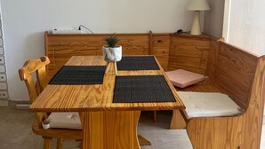 Una mesa de comedor de madera con un banco, una planta pequeña en maceta y una lámpara sobre una pared blanca.
