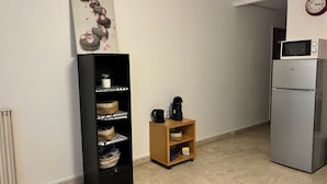 Una cocina equipada con microondas, refrigerador, cafetera y una estantería con cestas.