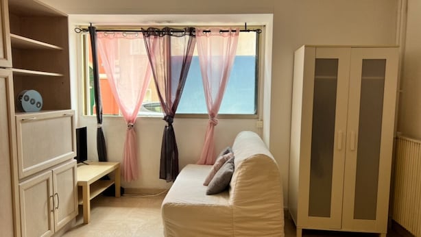 Una habitación con sofá, armario, ventana con cortinas translúcidas y vista al mar.