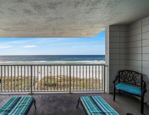 A balcony with a view of the ocean, two striped lounge chairs, and a bench with a blue cushion.