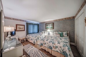 A hotel room with two beds, a desk with a lamp, a television, and a window with curtains. - FREE Golf & Perks! Mariner West 504 Beachfront Swimming Pool, Tennis & Grill! (Panama City Beach)