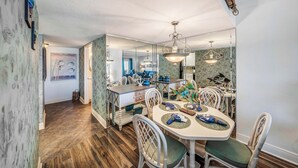 A dining area with a white table, green cushioned chairs, and a mirrored backsplash.