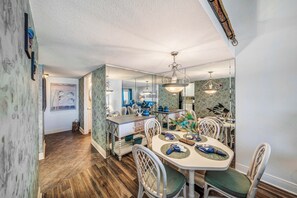 A dining area with a white table, green cushioned chairs, and a mirrored backsplash. - FREE Golf & Perks! Mariner West 504 Beachfront Swimming Pool, Tennis & Grill! (Panama City Beach)