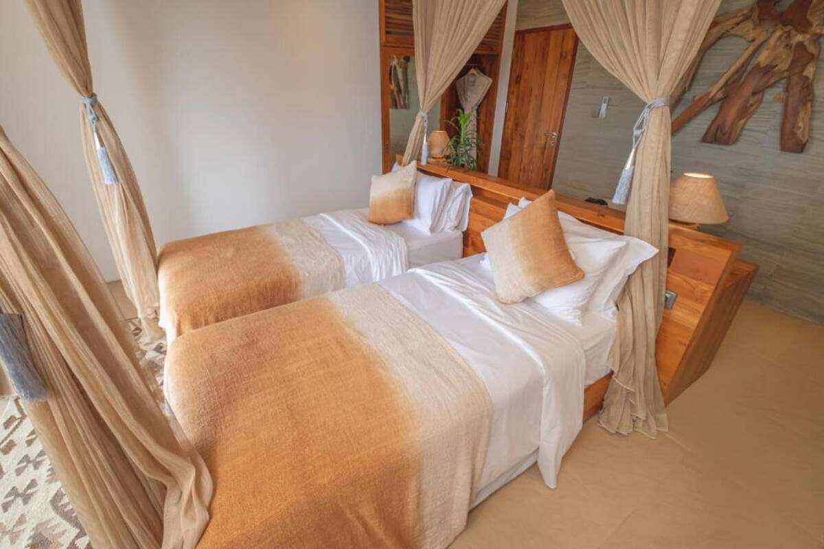 A double bed with beige and white bedding, a wooden nightstand, and a mirror.