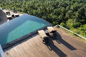 A wooden deck with a clear pool and lounge chairs overlooking a dense palm tree forest. - Villa Kalliste (Penida Island)