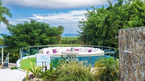 A circular infinity pool with white and purple cushions, surrounded by lush greenery and a stone wall. - 13 bedroom Ultimate Private Luxury Compound  with every amenity you can imagine (Sosúa)