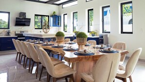 A modern kitchen with a large island, blue cabinets, and a dining area with a long wooden table and beige chairs. - 13 bedroom Ultimate Private Luxury Compound  with every amenity you can imagine (Sosúa)
