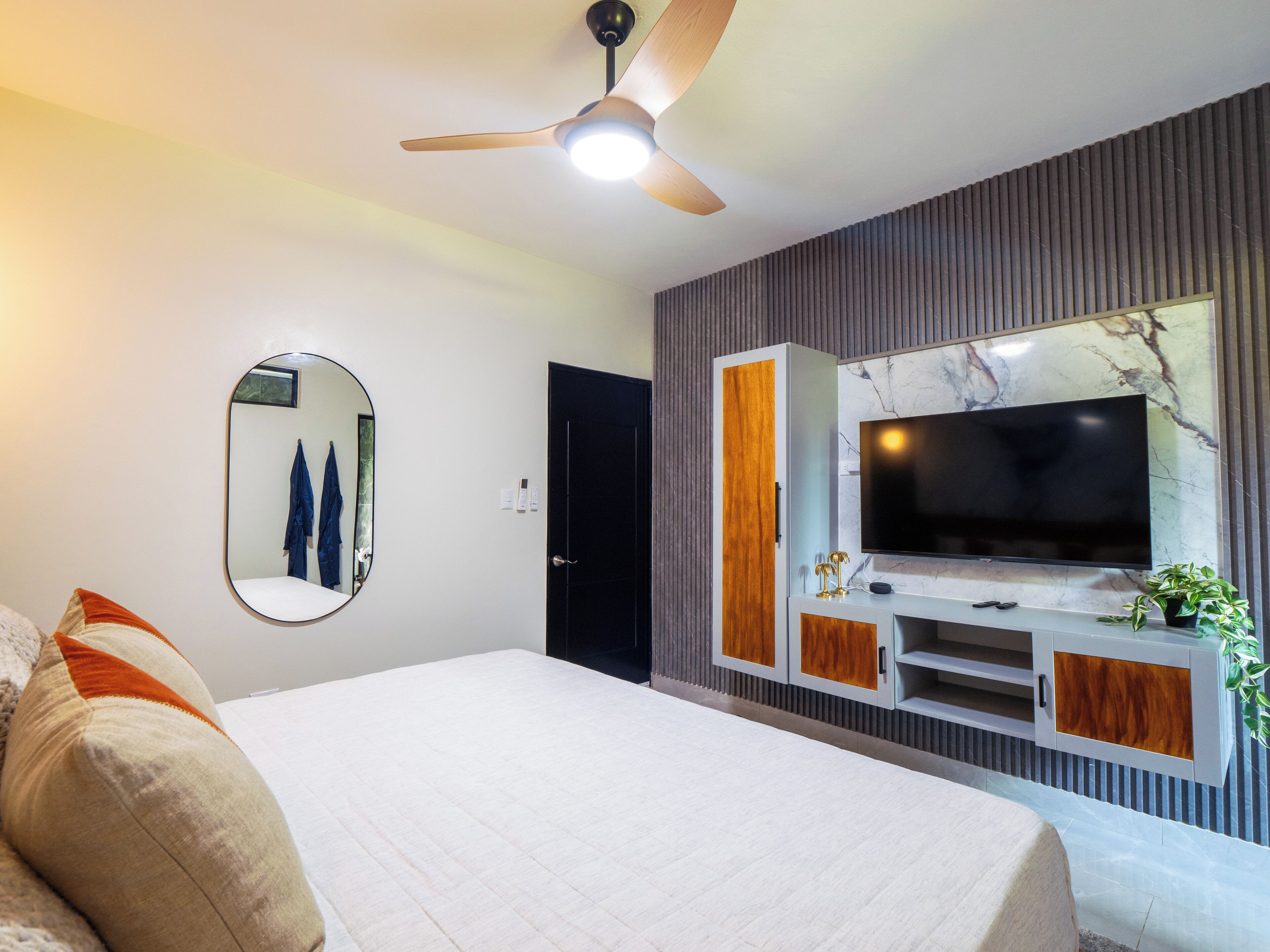 A modern bedroom with a bed, a ceiling fan, a TV, and a mirror.