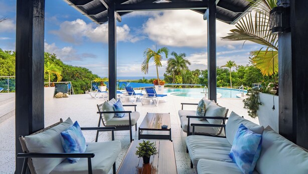A covered outdoor seating area with white sofas and chairs, a wooden table, and a pool in the background. - 13 bedroom Ultimate Private Luxury Compound  with every amenity you can imagine (Sosúa)