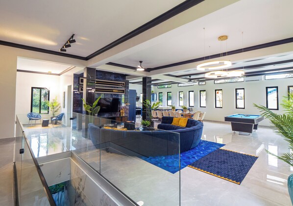 A spacious living area with a glass railing, a blue sofa, a pool table, and a flat-screen TV. - 13 bedroom Ultimate Private Luxury Compound with every amenity you can imagine (Sosúa)