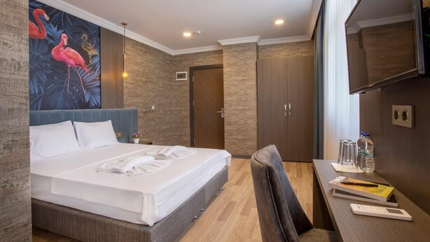 A hotel room with a large bed, a desk with a chair, a TV, and a painting of flamingos on the wall. - La Vie Suit Hotel (Istanbul)