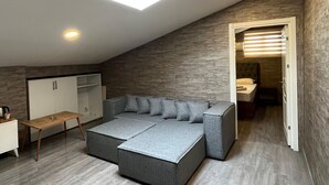 A modern loft bedroom with a large L-shaped sectional sofa, a desk, and a walk-in closet. - La Vie Suit Hotel (Istanbul)