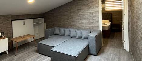 A modern loft bedroom with a large L-shaped sectional sofa, a desk, and a walk-in closet.