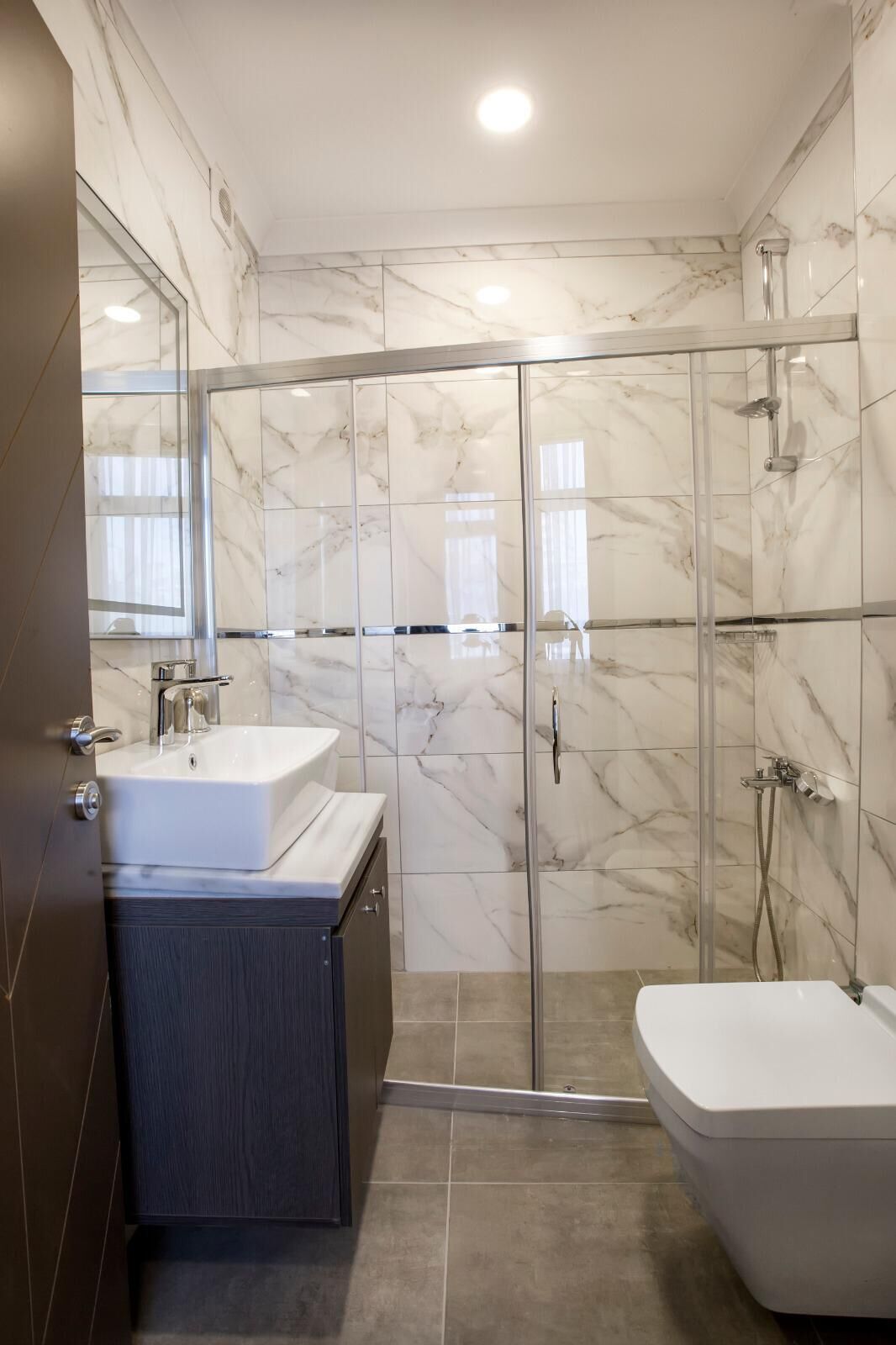 A modern bathroom with a glass-enclosed shower, a white sink, and a toilet.