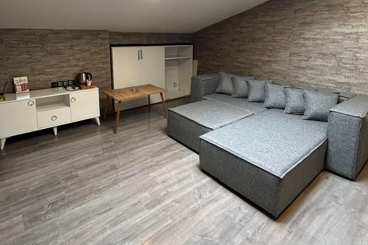 A modern, compact living space with a grey sectional sofa, a white wardrobe, and a wooden coffee table.