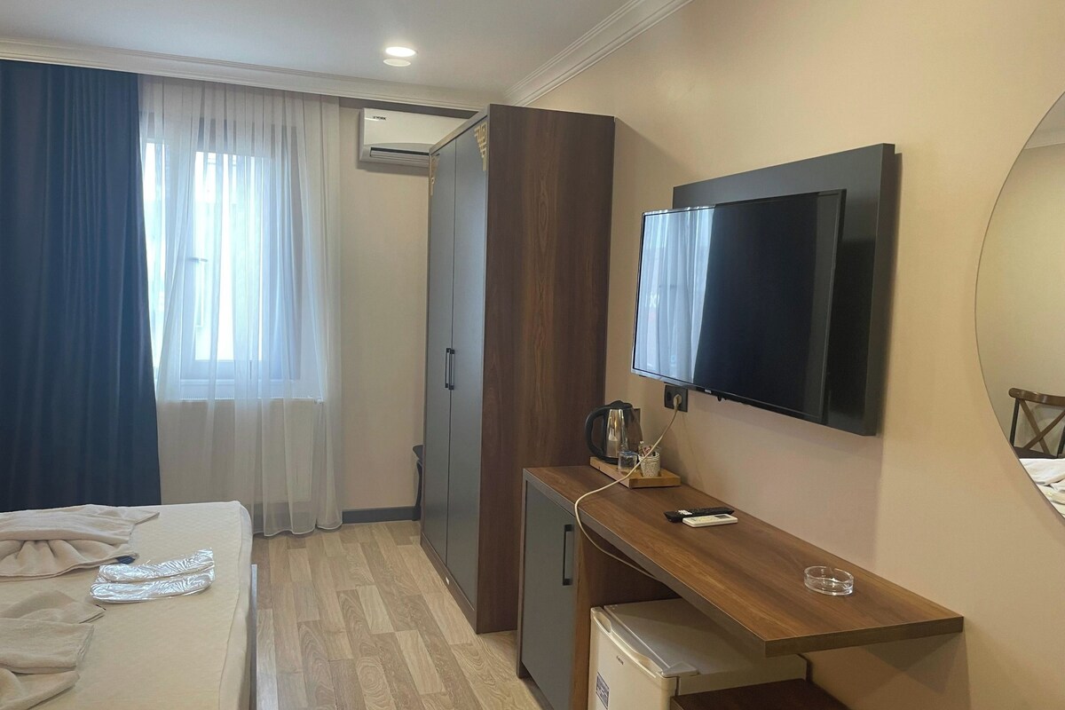 A hotel room with a bed, a desk with a television, a small refrigerator, and a wardrobe.