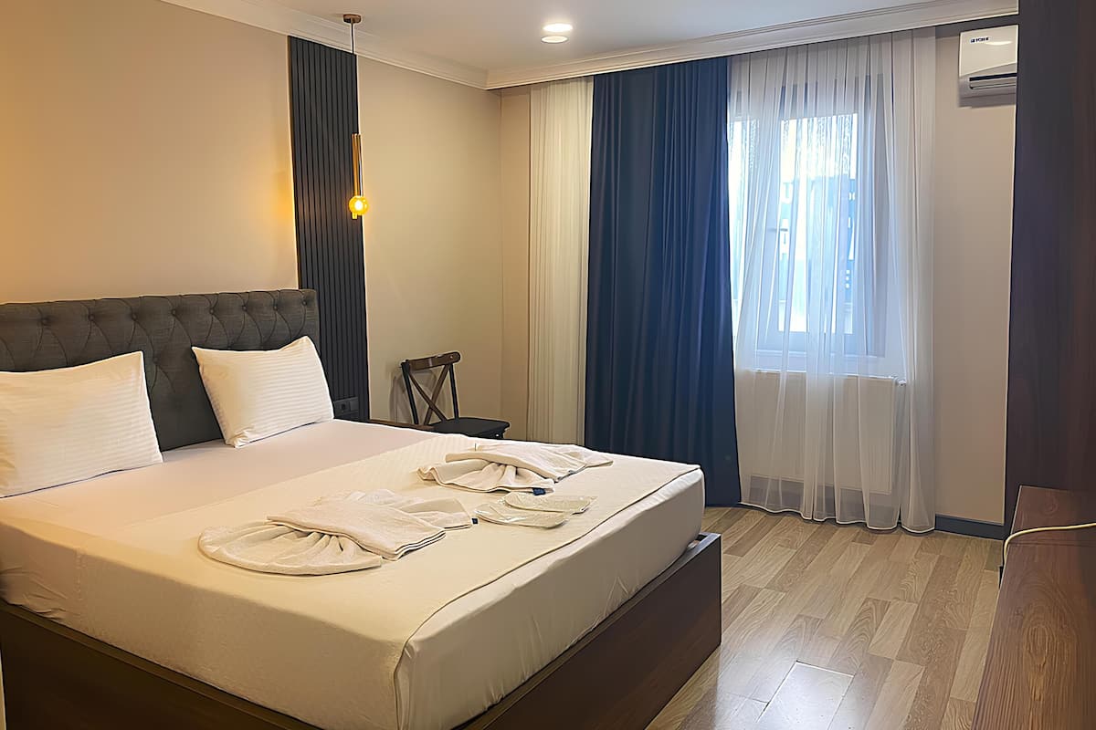 A hotel room with a large bed, a bedside table, a chair, and a window with curtains.