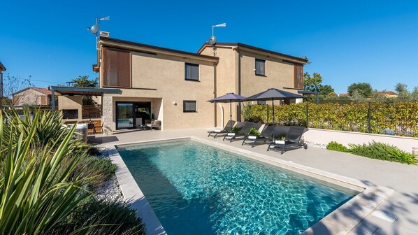 Una casa moderna con piscina, zona de estar al aire libre y jardín.