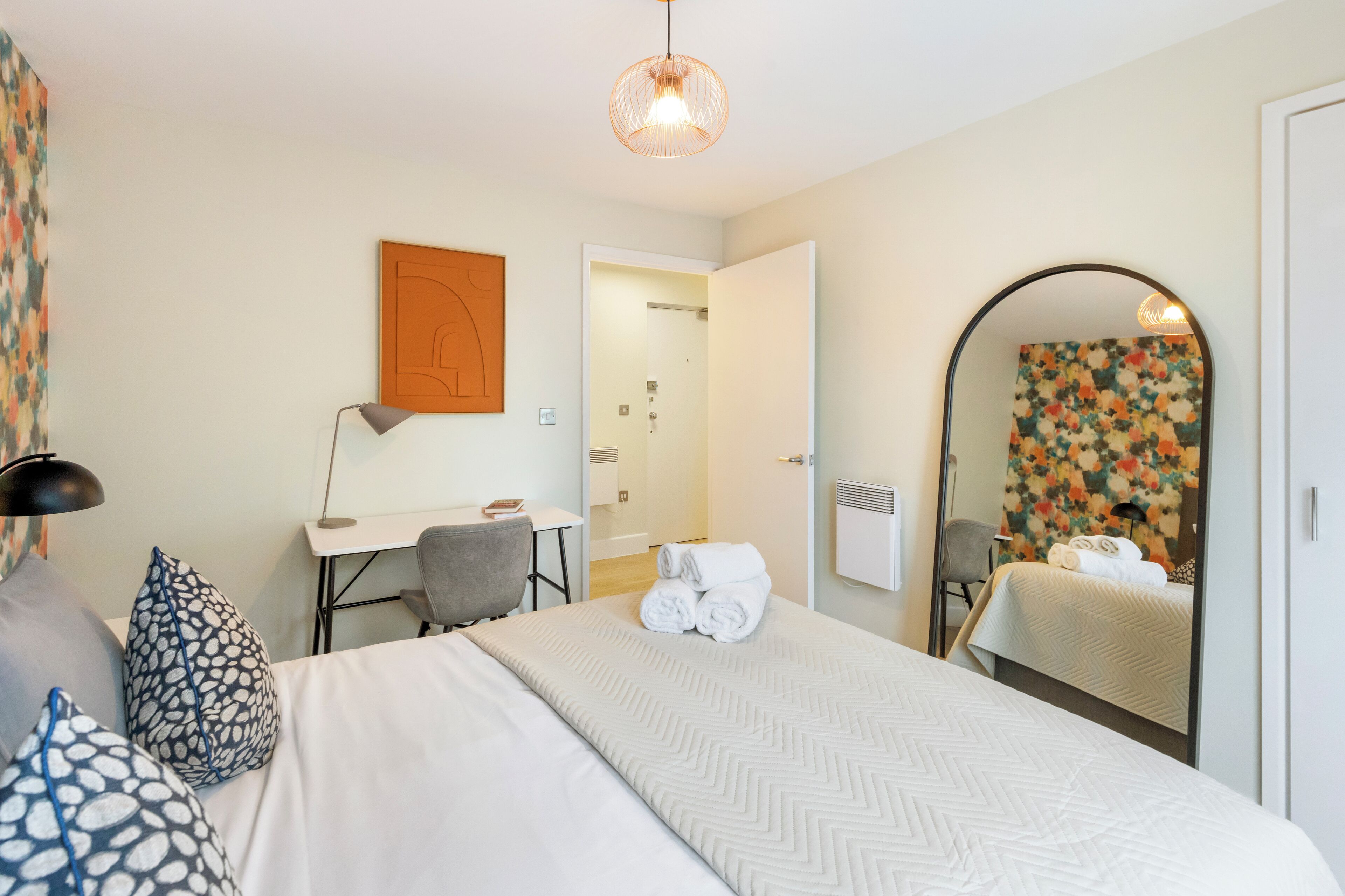 A hotel room with a bed, desk, chair, and a large mirror.