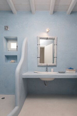A bathroom with a white sink, a mirror, and a shower. There is a small shelf with a decorative item and a light fixture above the mirror.