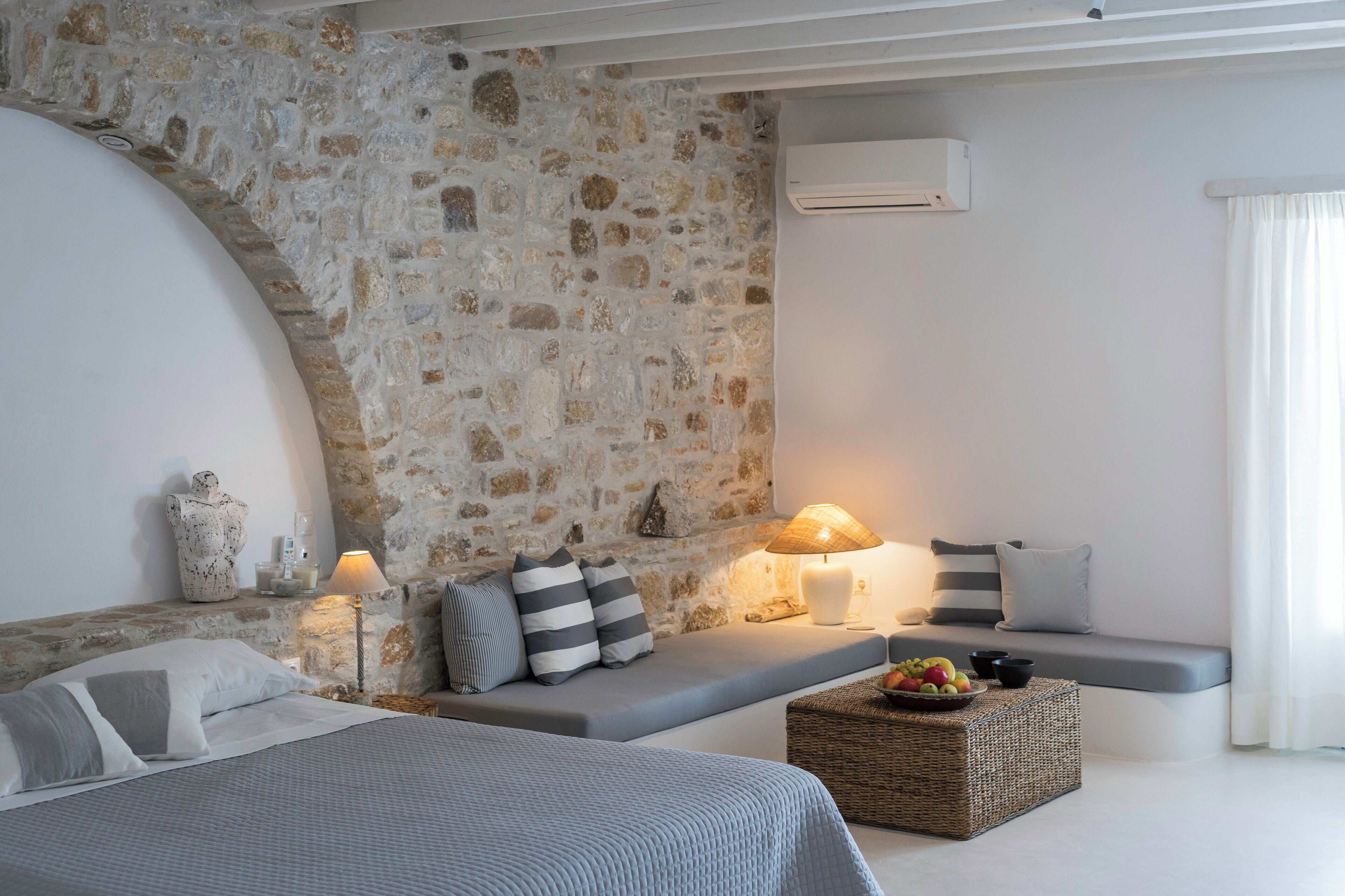 A modern bedroom with a stone wall, a bed, a sofa, a lamp, and a fruit basket.