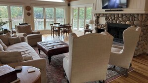 A spacious living room with a stone fireplace, comfortable seating, and large windows offering a view of the outdoors.