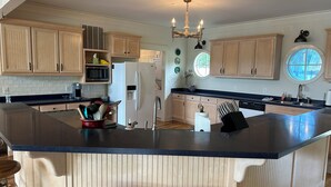 A kitchen with wooden cabinets, a central island with stools, a refrigerator, and a chandelier.