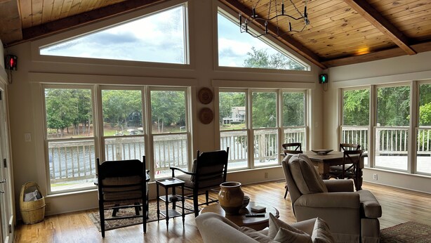 A spacious room with large windows, wooden flooring, and a cozy seating area with a sofa and chairs.