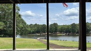 A covered outdoor area with a view of a lake, trees, and a dock.