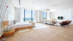 Une chambre d’hôtel moderne dotée d’un grand lit, d’un canapé, d’une télévision et offrant une vue sur la mer.