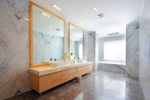 A modern bathroom with marble walls, a large mirror, dual sinks, and a trash bin.