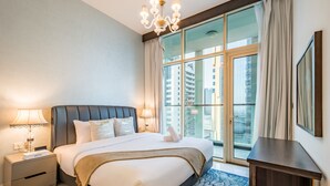 A hotel room with a large bed, a nightstand with a lamp, a dresser, and a view of tall buildings through the window. - Capacious 3BR Apartment in Bayz Tower, Business Bay by Deluxe Holiday Homes (Dubai)